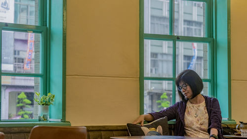 Side view of young woman sitting on window