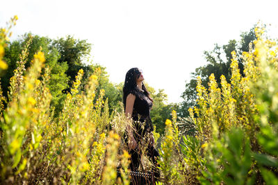 Woman standing by plants on field against sky