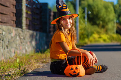 Portrait of smiling girl wearing hat sitting on road