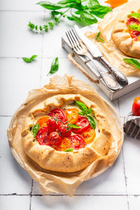 Fresh homemade galette with tomatoes, ricotta cheese and basil on white tile background.