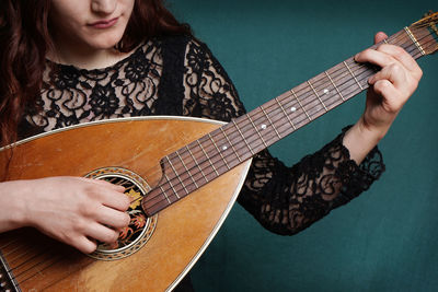 Midsection of woman playing lute against wall