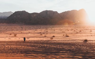 Silhouette man on desert by mountains against sky during sunset