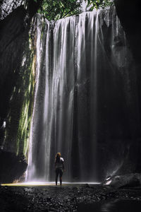 Full length of young woman standing against waterfall