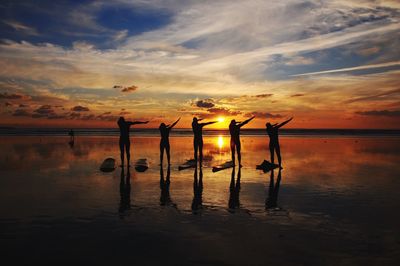 Silhouette people on beach against sky during sunset