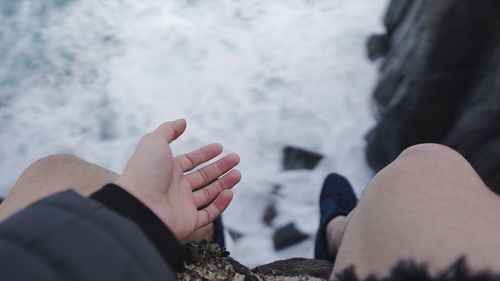 Low section of man sitting on cliff over sea