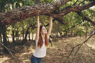 Portrait of young woman standing by tree trunk