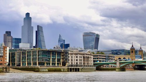 Modern buildings by river against sky in city