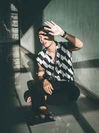 Man shielding eyes while sitting on tiled floor at home