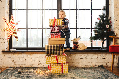 Boy stacking gifts against window at home