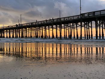 Pier over river against sky during sunset