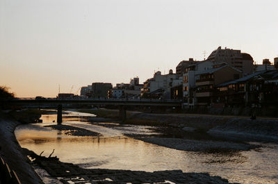 Bridge over river by buildings against clear sky