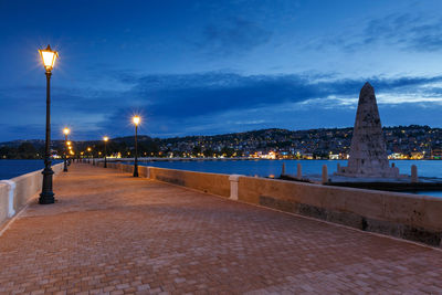 Illuminated street amidst buildings against sky at dusk