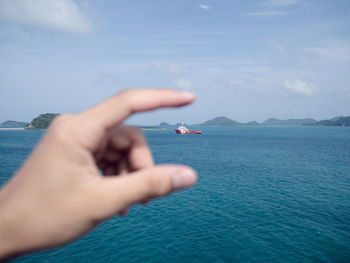 Cropped hand gesturing against boat in sea