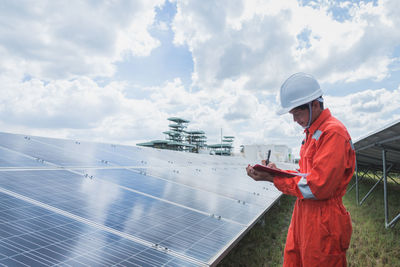 Engineer standing amidst solar panel against cloudy sky