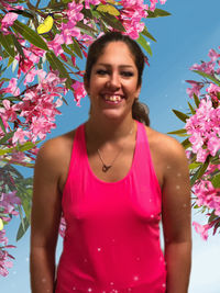 Beautiful young woman with pink flower standing against plants