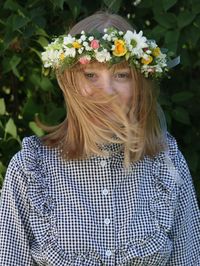 Portrait of woman wearing flowers standing against plants in park