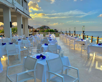 Chairs and tables at restaurant by sea against sky