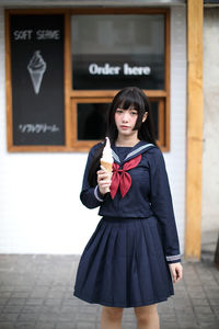 Portrait of smiling young woman eating ice cream standing outdoors