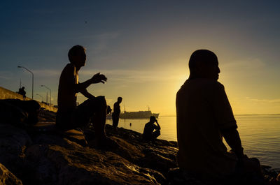 Silhouette men fishing at beach against sky during sunset