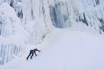 Female ice climber ascending snowy hill