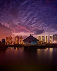 Illuminated buildings by river against sky at night