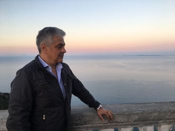 Man standing by sea against sky during sunset