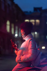 Young smiling african american woman with smartphone standing outdoors at night
