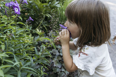 Small girl wearing a white blouse smelling lilac flower in a park