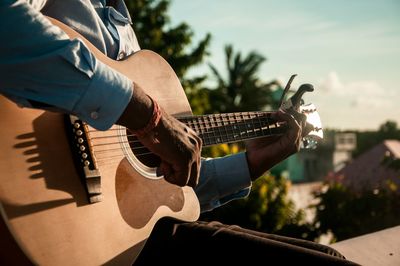 Midsection of man playing guitar on sunny day