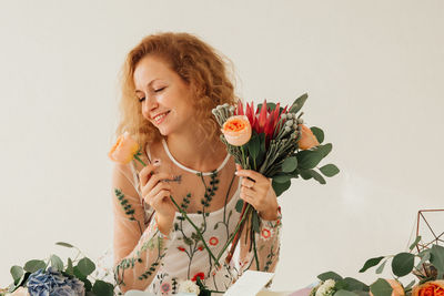 Young woman holding rose against white wall