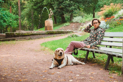 A girl and a labrador retriever sit on a bench in an empty park against the background of a fountain