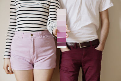 Midsection of woman holding color swatch while standing with man against wall at home