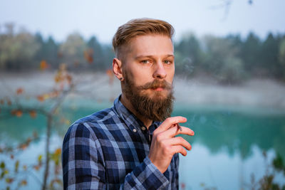 Smoking bearded man outdoors near lake in the evening. bad habit, addiction