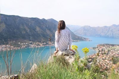 Rear view of woman sitting on rock against lake and mountains