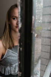 Close-up portrait of young woman looking through window at home