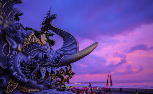 Statue at beach against sky during sunset