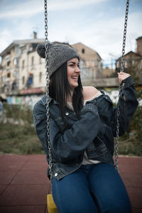 Young woman wearing denim jacket sitting on swing at playground