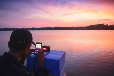 Man photographing camera at beach against sky during sunset