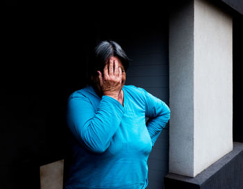 Woman covering face while standing against wall