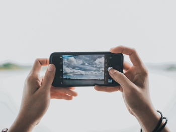 Cropped hand of woman photographing lake against sky