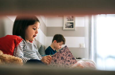 Siblings reading books on sofa at home