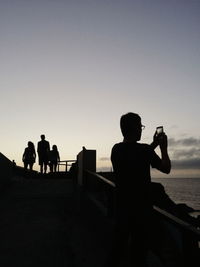 Silhouette people photographing on beach against clear sky