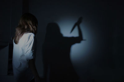 Woman looking at shadow with knife standing on wall