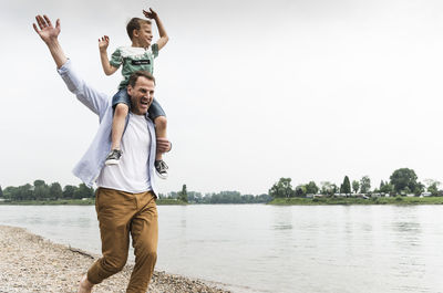 Happy father carrying son on shoulders at the riverside