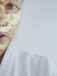 Cropped portrait of woman with golden facial mask over white background