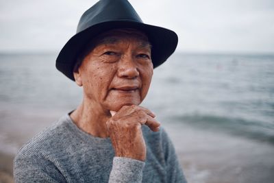 Portrait of senior man wearing hat standing at beach against sky during sunset