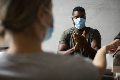 Female entrepreneur applying sanitizer while male colleague sitting by at office during pandemic