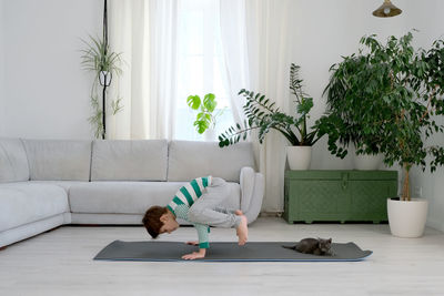 Cat sitting by boy exercising on mat at home
