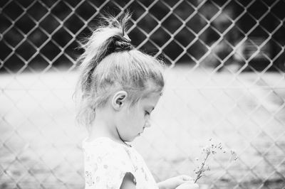 Close-up of girl holding flower while standing against chainlink fence