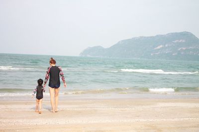 Rear view of women with daughter walking on beach against sky